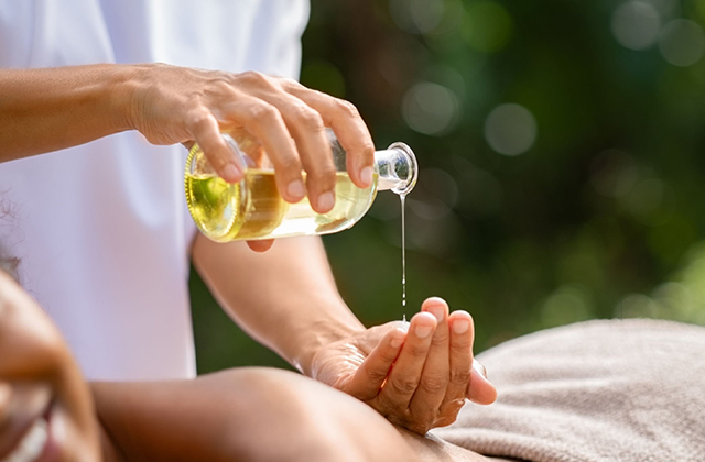 masseue is taking the body oil on her hand for massage 
